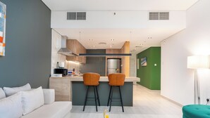 A modern living room with a sofa, a coffee table with fruit, and a kitchen area with two bar stools. - Samaya Holiday Homes - Marina luxury Suites (Dubai)