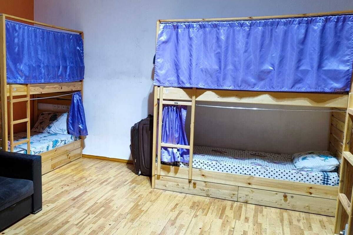 Quarto com duas beliches, piso de madeira e um sofá preto.