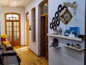 A hallway with wooden floors, a large teddy bear, a wall clock, and shelves with various items. - Sea Side Baku (Baku)