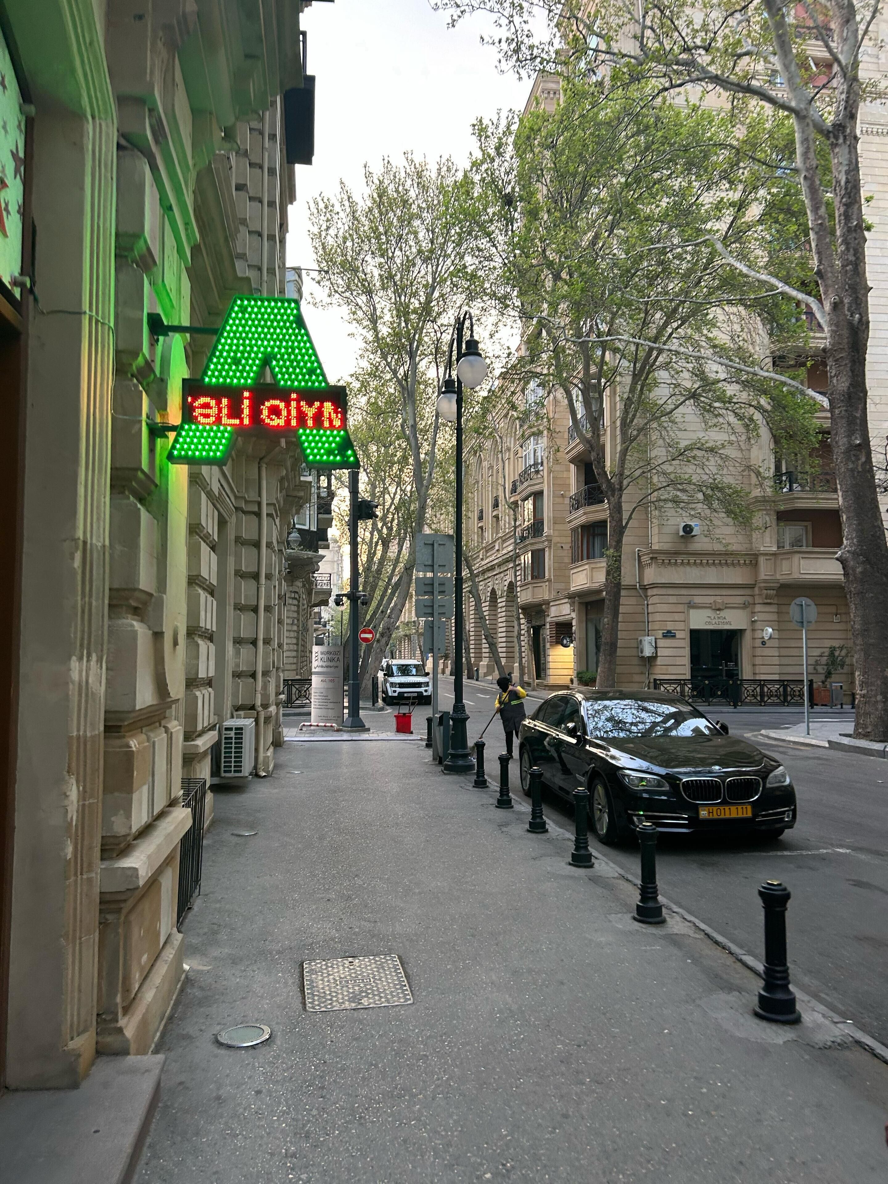 Eine Straße mit einem grünen Pfeilschild, einem parkenden Auto und Gebäuden im klassischen Stil.