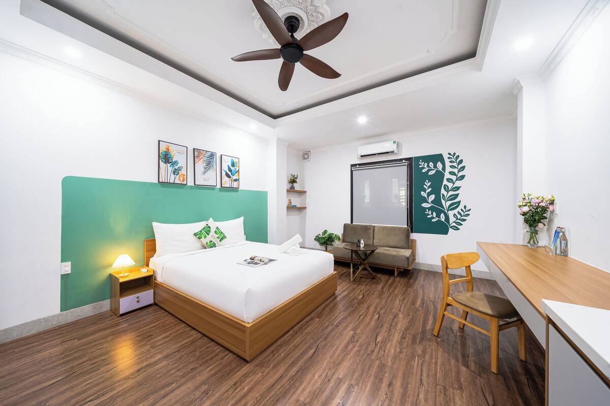 A modern bedroom with a bed, a desk, a chair, and a ceiling fan.