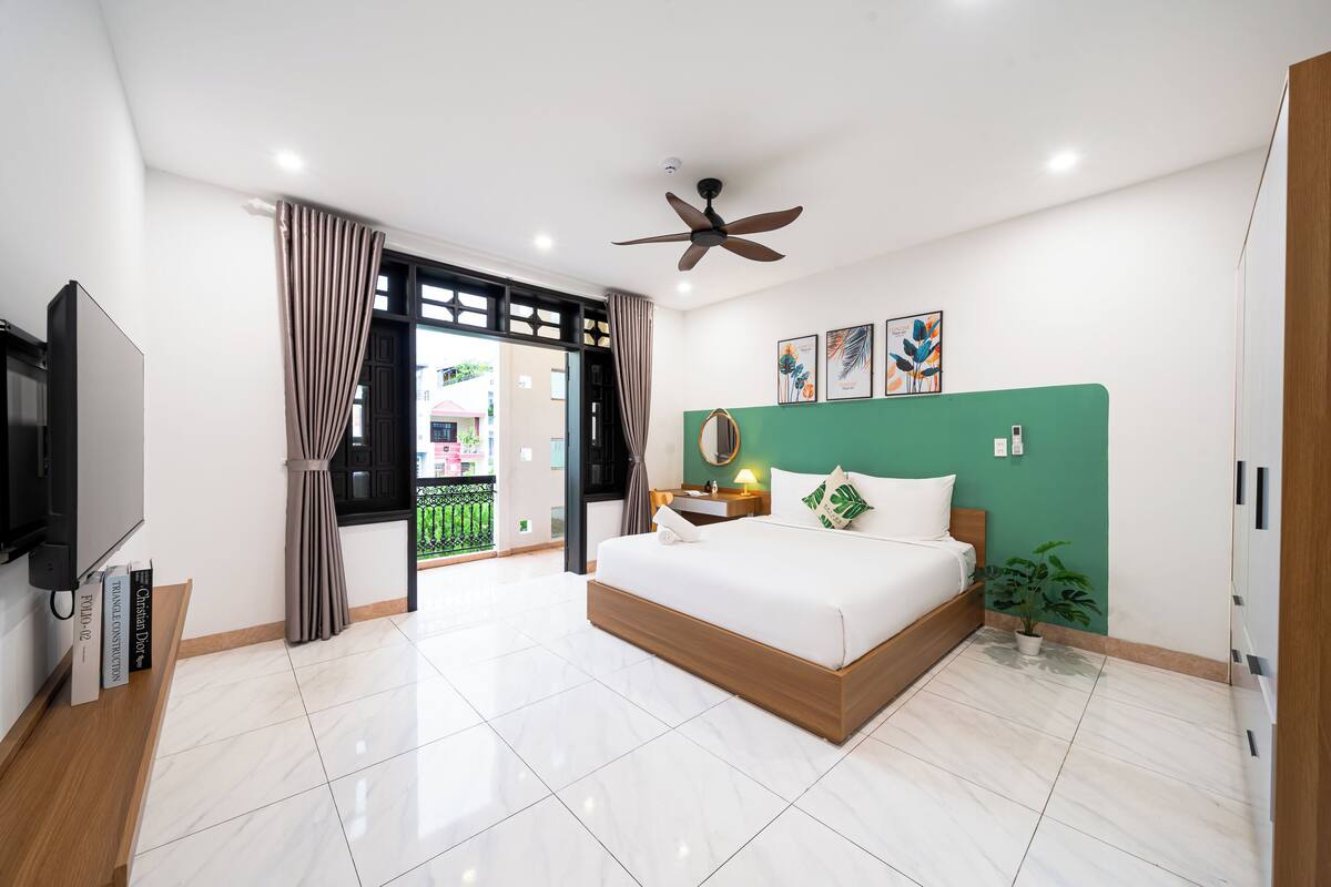 A modern bedroom with a large bed, a ceiling fan, a TV, and a balcony view.