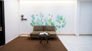 Ein Zimmer mit braunem Teppich, einem braunen Sofa, einem kleinen runden Tisch mit einem Buch und einer Wand mit einem Blatt-Wandgemälde.