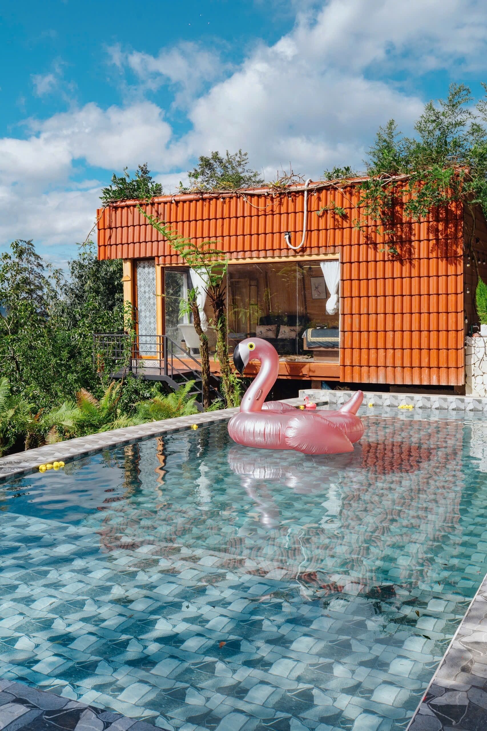 Un edificio moderno con piscina, un gonfiabile a forma di fenicottero rosa e vegetazione lussureggiante.