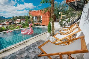 Una piscina con un flotador de flamenco rosa, sillas de descanso de madera y vistas del entorno.