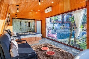 Una habitación de madera con una cama, un sofá y un ventanal con vistas a una piscina que tiene un flotador con forma de flamenco.