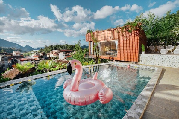 Una piscina con un flotador de flamenco rosa, rodeada por un muro de piedra y una terraza de madera.