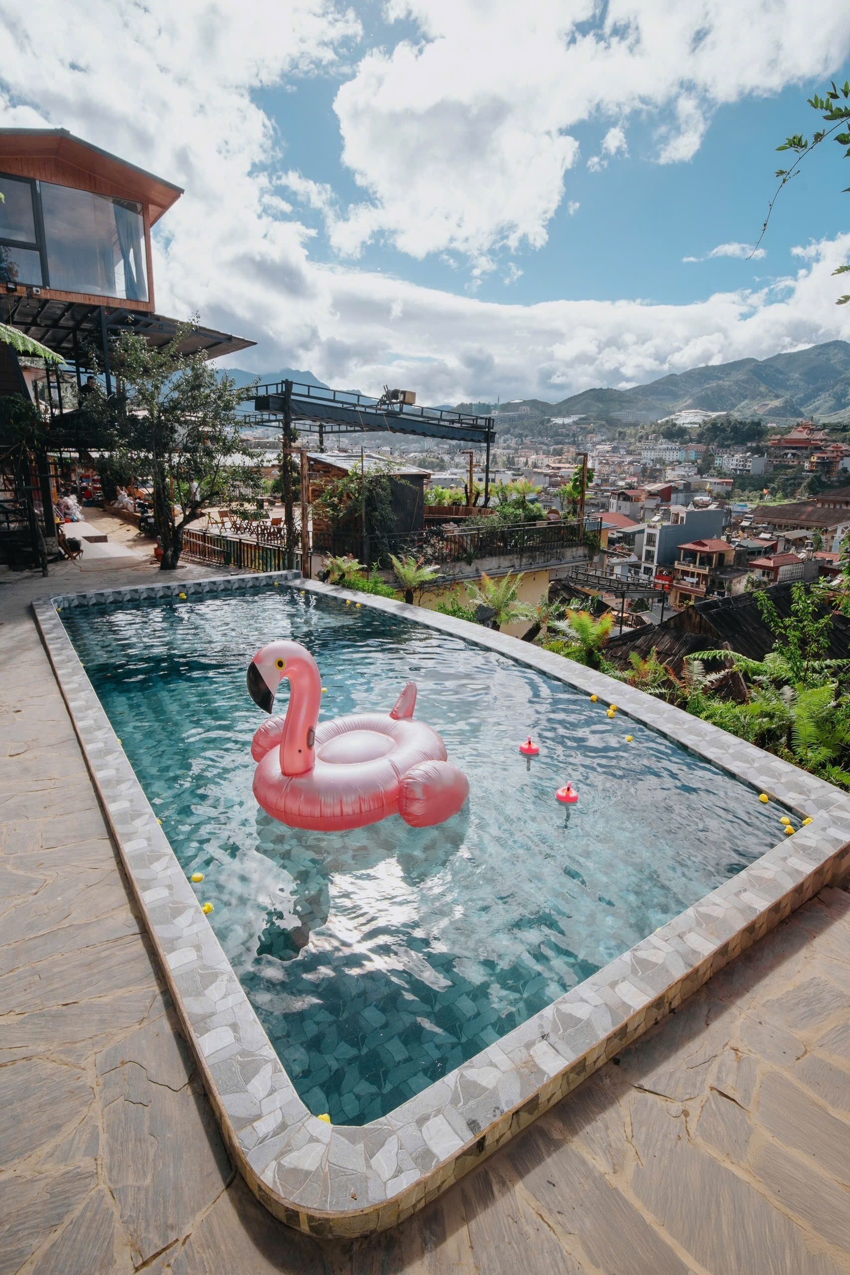 Una piscina con un flotador de flamenco rosa, rodeada de baldosas de piedra y vistas a un paisaje urbano y montañas.