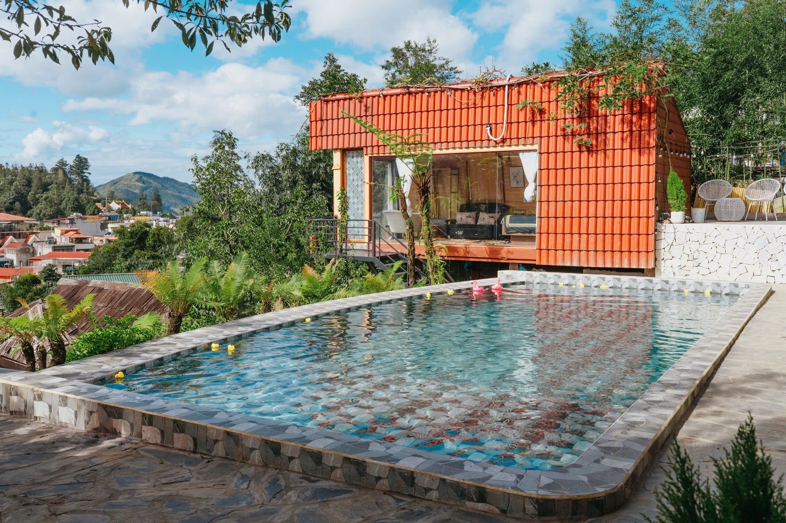 Une maison moderne avec une piscine, entourée de verdure et avec des montagnes en toile de fond.