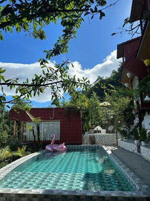 Una piscina con un flotador de flamenco rosa, rodeada de baldosas de piedra y follaje.