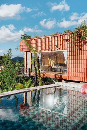 Un edificio moderno con fachada de vidrio, una piscina y abundante vegetación.