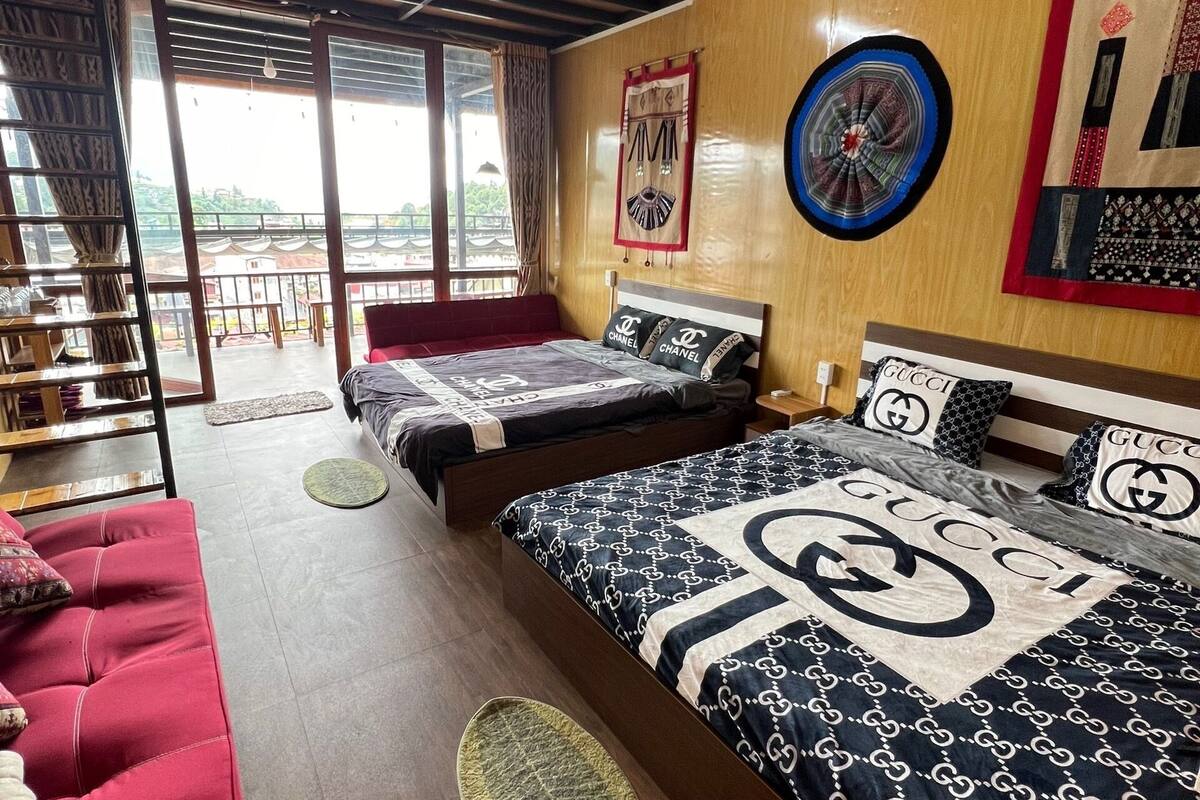 A hotel room with two beds, a red sofa, a balcony, and a view of the city.