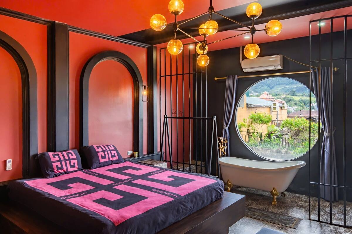 A modern bedroom with a large bed, a vintage bathtub, and a view of a cityscape through a large window.