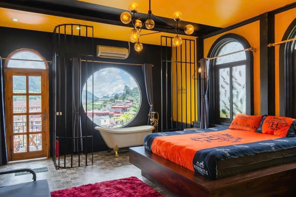 A bedroom with a large bed, a round window, a bathtub, and a view of the city.