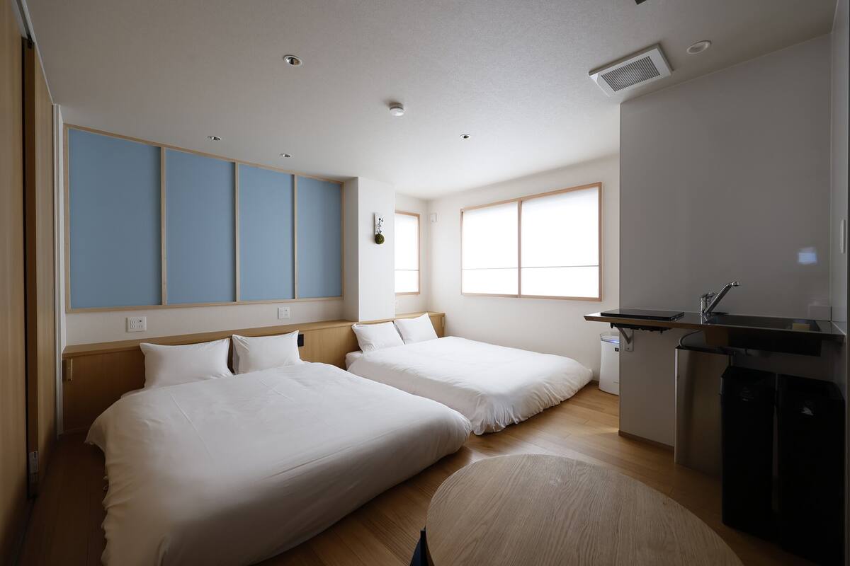 A hotel room with two beds, a kitchenette, and a large window.