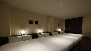Habitación de hotel con dos camas, cada una con una mesita de noche y una lámpara. La habitación tiene un armario de madera oscura y paredes color beige.