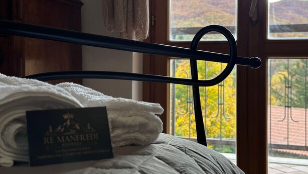 Ein Bett mit einem gefalteten weißen Handtuch und einer Karte mit dem Schriftzug „RE MANFREDI“.