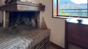 Ein Zimmer mit Kamin aus Stein, einem Fenster mit Bergblick und einer Holzkammer mit diversen Gegenständen.