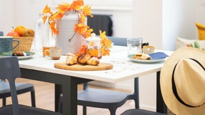 Una mesa de comedor con sillas, una cafetera, un jarro y una cesta de naranjas.