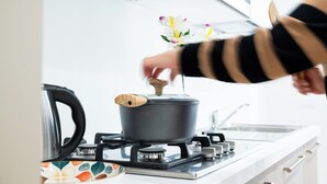 Una cocina con estufa a gas, una olla en la hornilla y una mano ajustando la tapa.