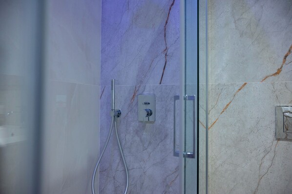 Un baño con cabina de ducha de vidrio, paredes de mármol y panel de control a la vista.