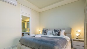A bedroom with a large bed, a nightstand with a lamp, and a mirror above the bed. - Crest - 3 Bedroom Apartment in Hamra (Beirut)