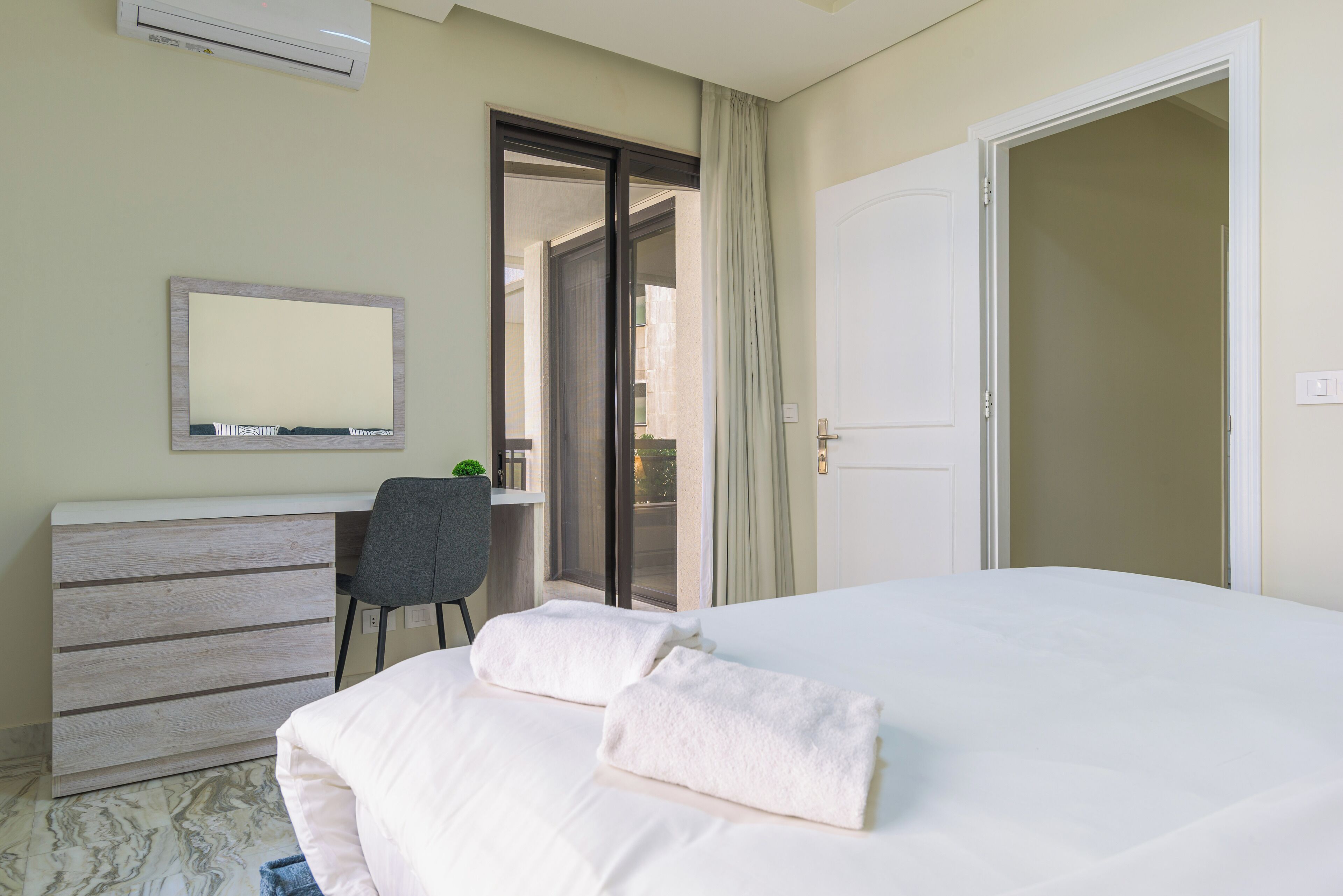 Una habitación de hotel con cama, escritorio, silla y puerta que da a un balcón.