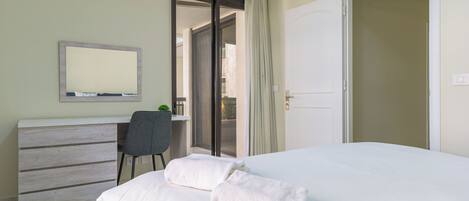 Una habitación de hotel con cama, escritorio, silla y puerta que da a un balcón.