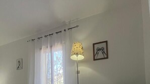 Ein Wohnzimmer mit einem grünen Sofa, einem Glastisch, einer Stehlampe, einer Heizung und einem Fenster mit transparenten Vorhängen.