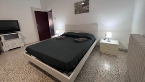 Ein Schlafzimmer mit Bett, Fernseher, Nachttisch und Tür.