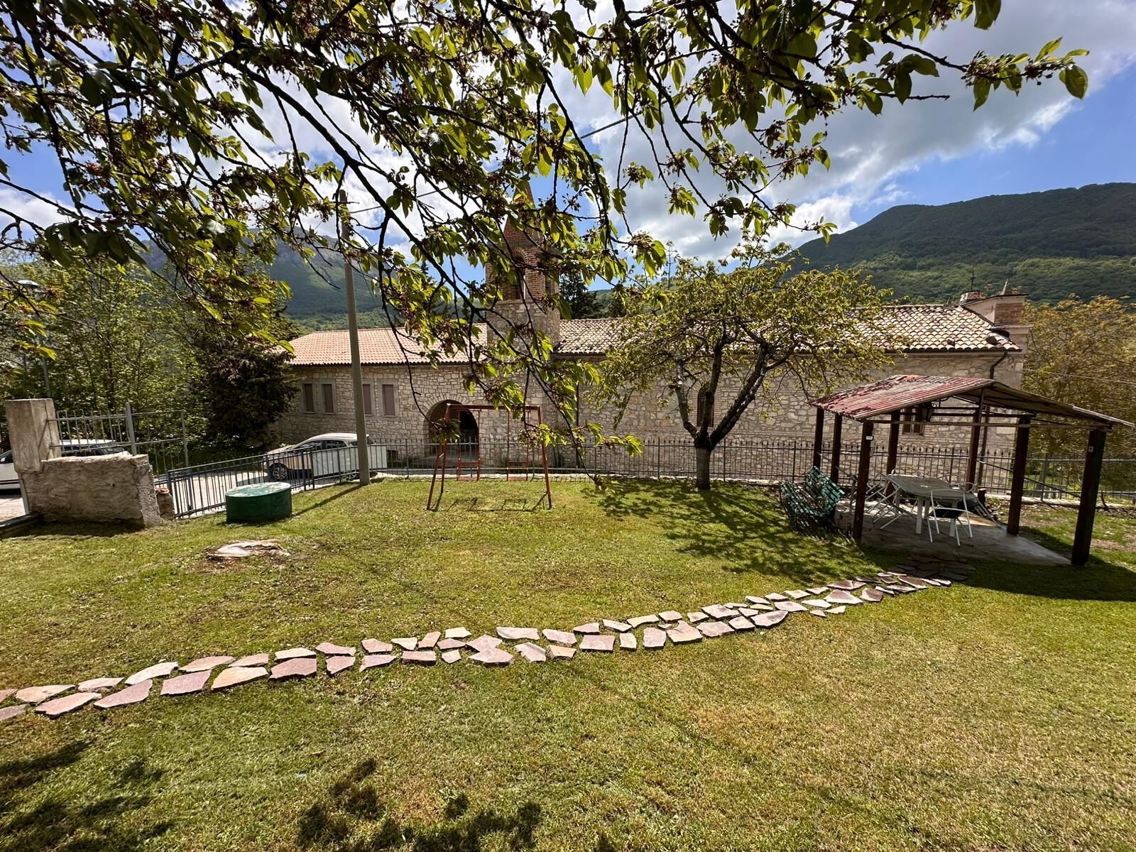 A stone building with a tiled roof, a grassy yard, a stone pathway, and a gazebo.