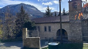 Ein Steingebäude mit einem Turm, einer gepflasterten Fläche und einem Berg im Hintergrund.