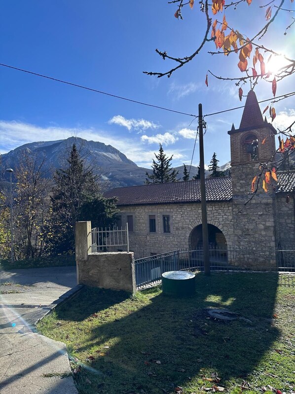 A stone building with a tower, a paved area, and a mountain in the background.