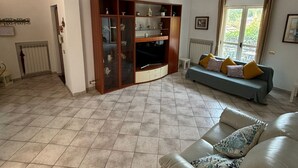 A spacious living room with a large wooden entertainment unit, a grey sofa with patterned cushions, and a tiled floor. - VESUVIUS GARDEN 10 MINUTES FROM POMPEI (Boscoreale)