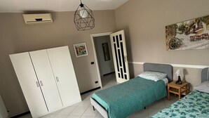 A bedroom with two beds, a wardrobe, a door, a ceiling light, and a wall-mounted air conditioner. - VESUVIUS GARDEN 10 MINUTES FROM POMPEI (Boscoreale)