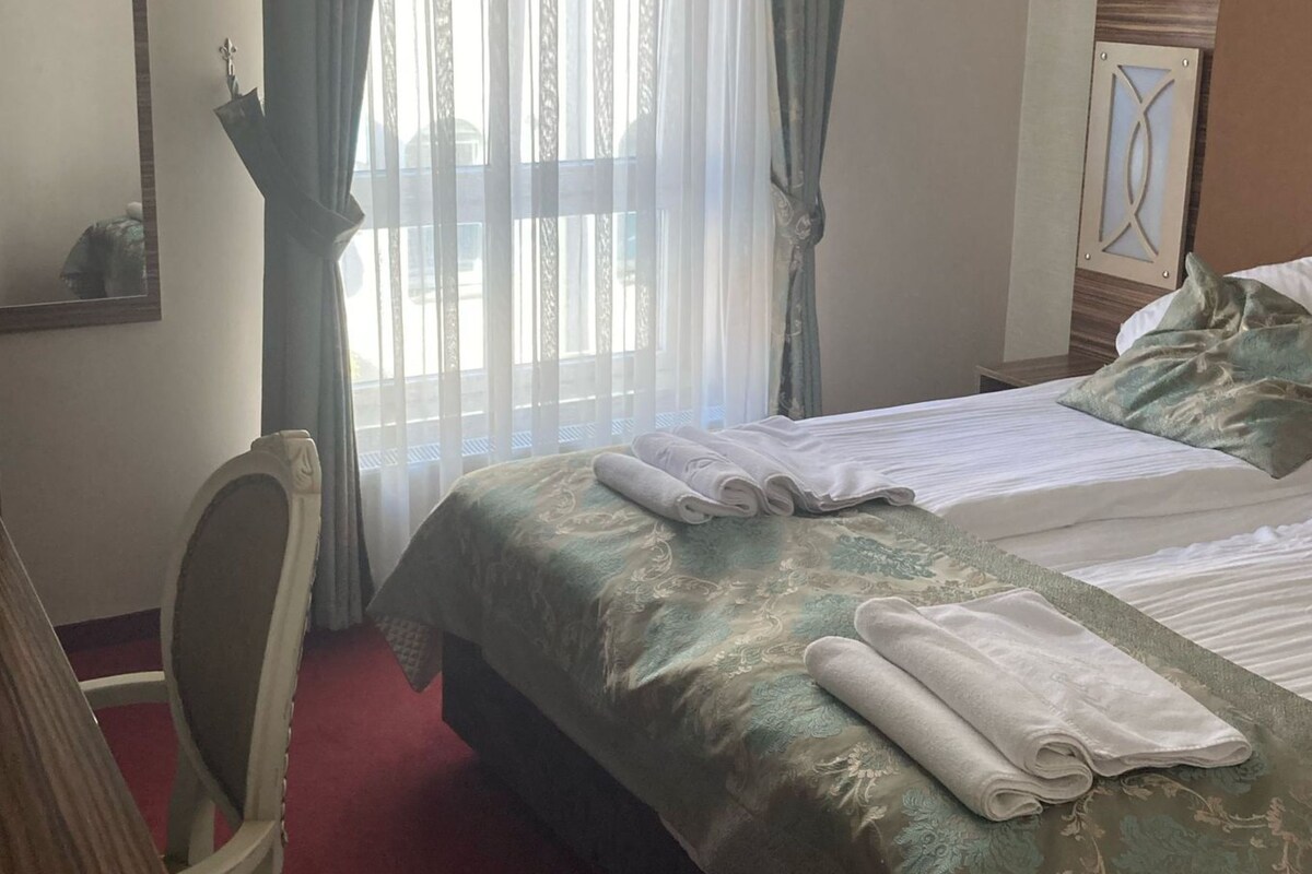 A hotel room with a bed, a desk, a chair, and a window with curtains.