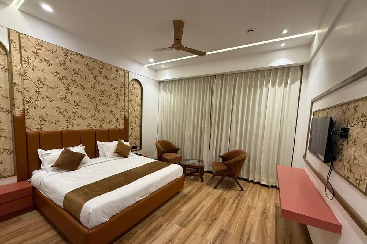 Habitación de hotel con una cama grande, dos sillones, una mesita, televisor y ventilador de techo.