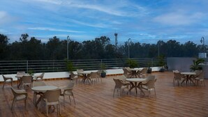 Terraço no telhado com mesas redondas e cadeiras de vime, ladeado por um corrimão e vista para uma área arborizada.