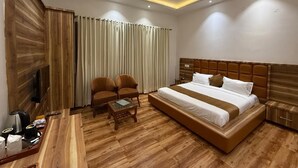 Quarto de hotel com uma cama grande, duas poltronas, uma mesa de centro, televisão e ventoinha de teto.