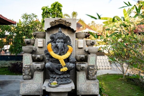 A stone structure with a deity figure, surrounded by greenery and a tiled roof in the background. - Karang Mas Villa Lembongan (Lembongan Island)