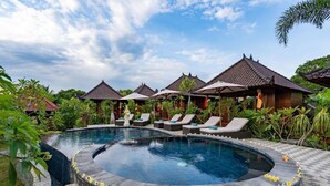 A circular pool with lounge chairs and umbrellas, surrounded by tropical vegetation and traditional-style buildings. - Karang Mas Villa Lembongan (Lembongan Island)