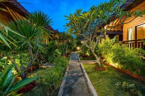 A pathway leading to a row of wooden buildings with a lush garden on either side. - Karang Mas Villa Lembongan (Lembongan Island)