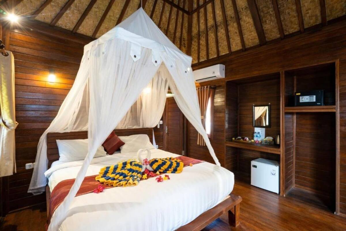 Una habitación con una cama bajo un dosel, paredes de madera, un televisor pequeño y un armario blanco.