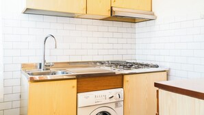 Eine kleine Küche mit Holzschränken, einer Edelstahlspüle und einer integrierten Waschmaschine.