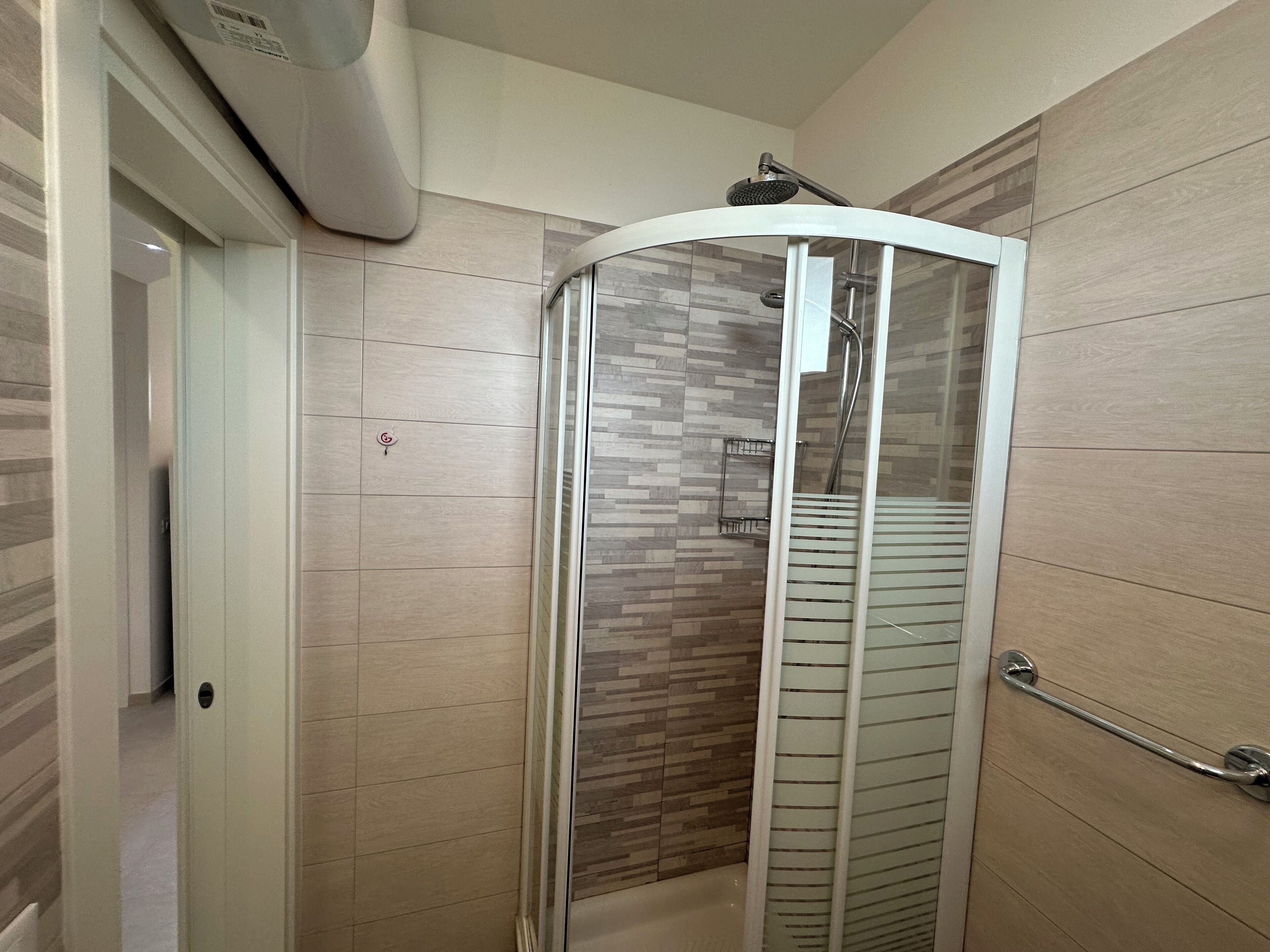 Un bagno moderno con doccia in vetro, pareti piastrellate e porta bianca.