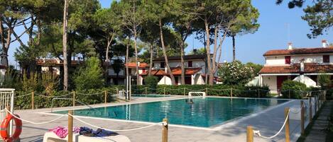 A swimming pool with a wooden deck, surrounded by trees and buildings.