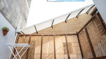 A covered outdoor area with a bamboo screen, a white folding table, and a potted plant.