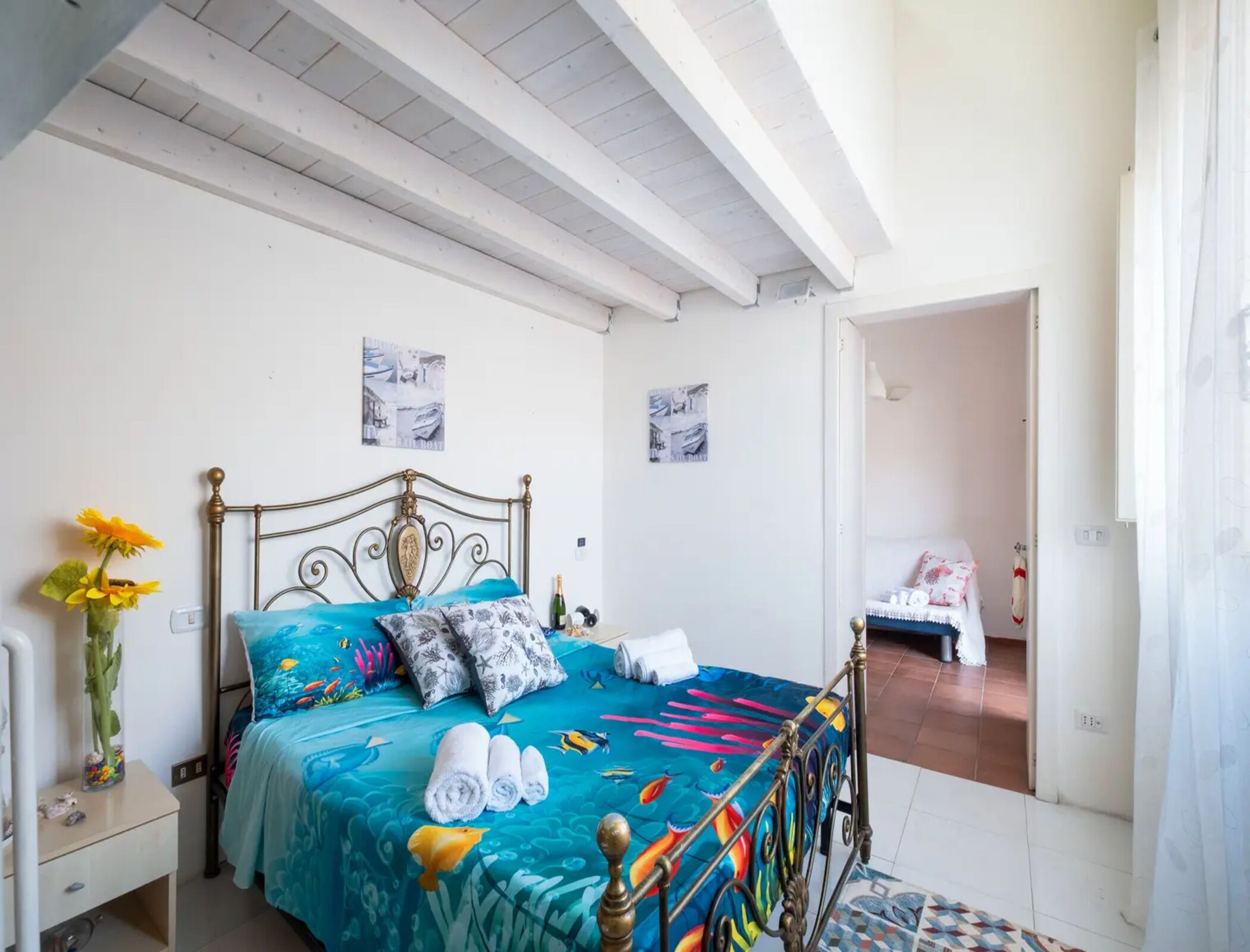 A bedroom with a bed, a nightstand, a vase with flowers, and two wall art pieces.