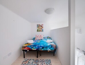 A small, brightly lit room with a bed, a colorful rug, and a painting on the wall. - Vista Sul Blu Private Residence 3 (Porto Cesareo)