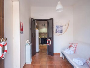A hallway with a door leading to a kitchen, a bench with towels, and a life preserver on the wall. - Vista Sul Blu Private Residence 3 (Porto Cesareo)